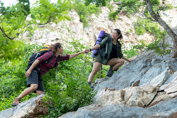 Group Hiker woman helping her friend climb up the last section of sunset in mountains. Traveler...