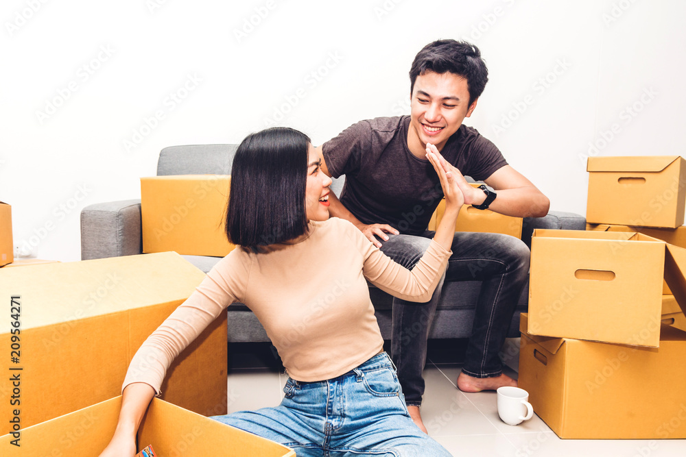 Wall mural Happy young couple giving high-five and unpacking box and moving into their new home.House moving and real estate concept