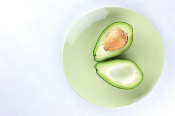 Avocado on white background, sliced avocado on green plate, vegetarian food, mexican food, tropical fruit for breakfast, copy space