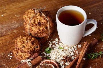 Christmas concept with a cup of hot tea, cookies and decorations on a log over wooden background, selective focus