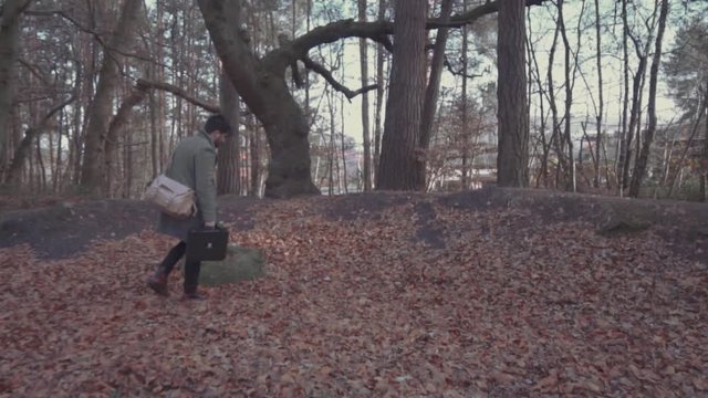 Man walks through forest in autumn with suitcases 