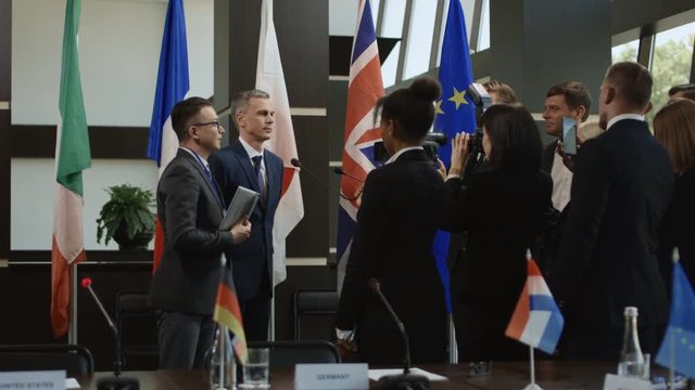 Formal representative standing against international flags and communicating with press media giving interview