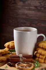 Christmas concept with a cup of hot tea, cookies and decorations on a log over wooden background, selective focus