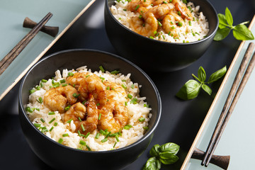 Two bowls of black color with rice and fried shrimp on a blue table. Asian food.