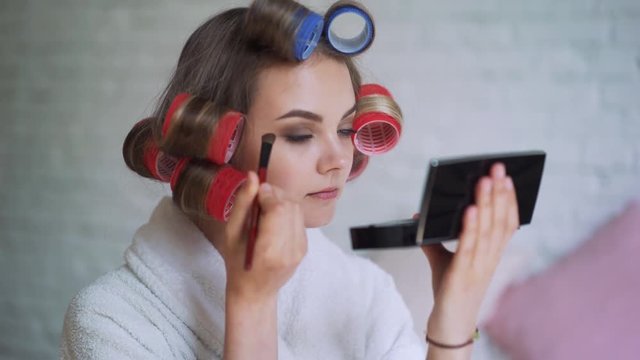Makeup young woman putting lipstick wearing hair rollers getting ready for going out.
