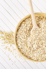 Oatmeal flakes in a wooden bowl on a white background. A wooden spoon in a bowl with porridge. Vertically.