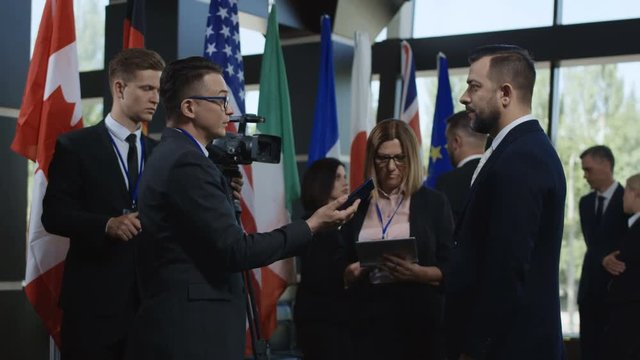 Side view of social media agents taking interview from male politician on international meeting