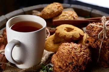 Conceptual festive composition with a cup of hot tea, cookies and spicies on a wooden barrel, selective focus, close-up