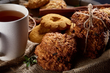 Conceptual festive composition with a cup of hot tea, cookies and spicies on a wooden barrel, selective focus, close-up