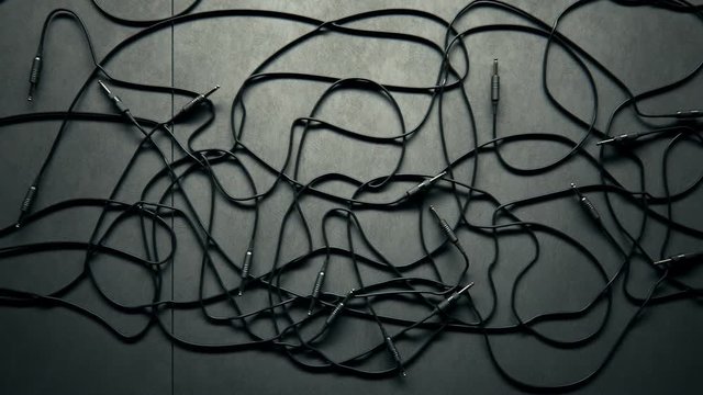 Bunch of tangled black audio cables with jack plugs lying on grey studio floor.