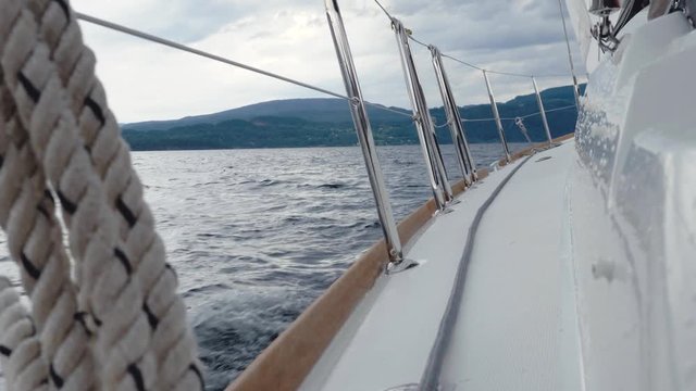 Close-up of thick rope coiled on ship railing. Large drops of rain on surface of yacht deck. Someone or something standing on side deck by white motor boat, enjoying magnificent scenery, during cruise