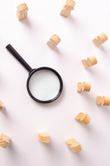 A magnifying glass lies in the center of the wooden figures of people who look at it. The concept...