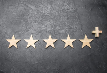 Five wooden stars and a plus, on a concrete gray background. The concept of the highest evaluation...