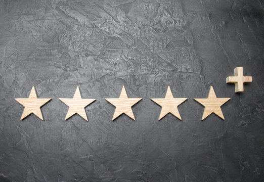 Five wooden stars and a plus, on a concrete gray background. The concept of the highest evaluation of quality and service. Better than five stars. Excellent performance and stunning success.