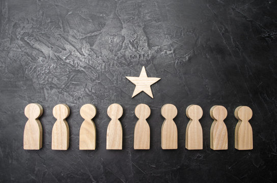 A star above a person who stands in a row among other people. Wooden figurines. The concept of a sign of distinction, success, achievement and career growth. Promotion, the best worker.