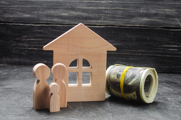 Wooden figures of the family stand near a wooden house and collapsed money. Buying and selling a house. Good life, moving to new apartments. Realtor services. A happy family.