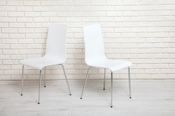 White chairs near the white wall for interior or graphic backgrounds. The chairs can be used to represent interview sessions or waiting rooms for ads purpose.
