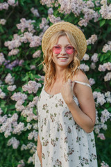 portrait of a beautiful young girl in a white dress in a hat and pink glasses on the background of...