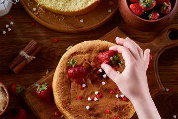 Close up of girl's hands decorating top of delicious strawberry cake, close up, selective focus.