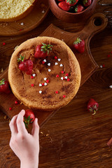 Close up of girl's hands decorating top of delicious strawberry cake, close up, selective focus.