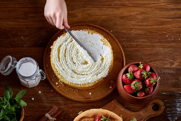 Close up of girl's hands adding cream on top of delicious strawberry cake, close up, selective focus.