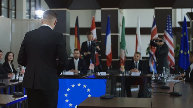 Back view of man giving speech in front of multicultural representatives on European union negotiation in boardroom