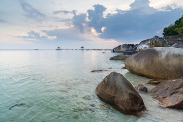 Crystal clear water and big rocks on the beach of Tioman island. Boat jetty and boat in the background. Malaysia