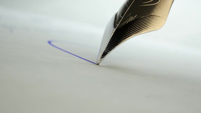 Close up of a quill pen writing a letter with blue ink. Calligraphy, handwriting