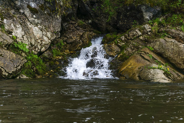The spring follows a waterfall from the rock and flows into the river on a precipitous river bank