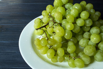 Ripe grapes in a plate on a dark blue wooden table.