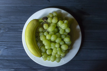 Ripe grapes and bananas in a plate on a dark blue wooden table.