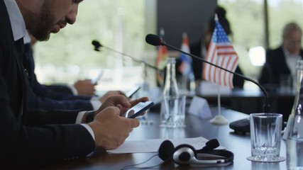 Crop side view of men sitting at table of international conference and using smartphones in break
