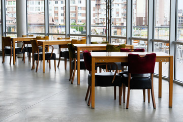 Empty wooden tables and leather chairs stand near the panoramic windows. Food court.