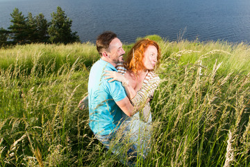 Couple in love passionately hug. Long-awaited meeting of the two lovers outside near of lake. Red hair woman and man hug in the grass