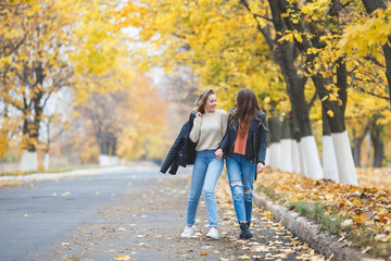 Young pretty girls having fun outdoors in autumn background. Cheerful friends in the fall time