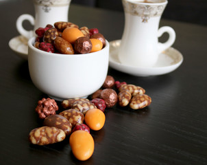 Chocolate sweets in a bowl and two cups of coffee on a table.