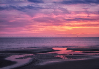 beautiful near dark twilight over a calm flat sea with purple sky and blue clouds reflected in water on the beach
