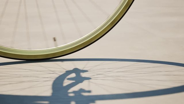Road bike wheel spinning and casting shadow over a concrete road. Loop animation