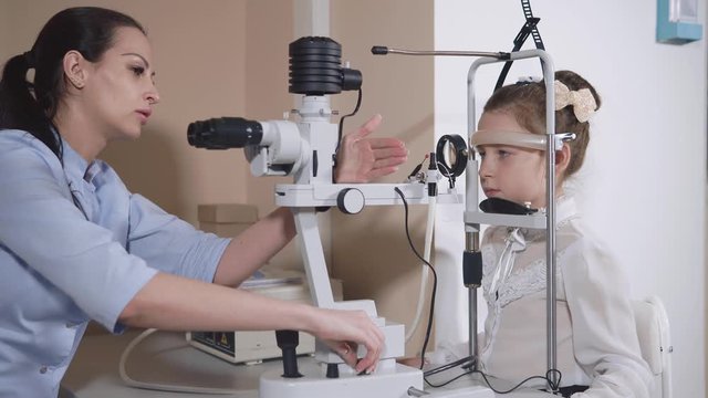 Side view shot of a female ophthalmologist working with young girl. She is using slit lamp for examining her eyes.