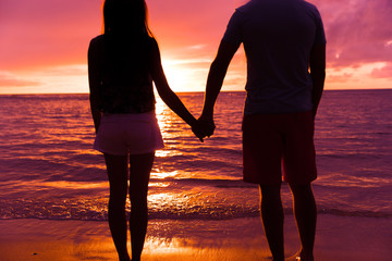 Beach honeymoon vacation couple in love holding hands at sunset on Caribbean travel. Silhouettes against sun flare sunlight at sunrise.