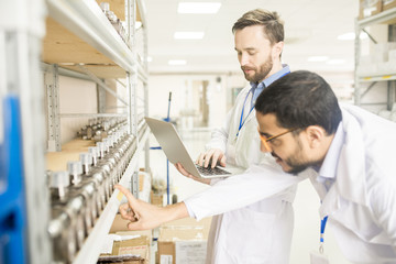Multi-ethnic group of engineers wearing lab coats examining quality of measuring equipment while carrying out inspection at warehouse of modern factory - obrazy, fototapety, plakaty