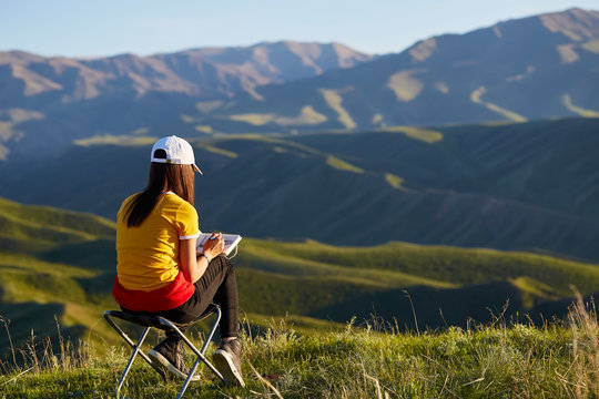 A girl in the background of mountains drawing a landscape. Sits with his back. Painting outdoors. Kazakhstan. Mountain landscape