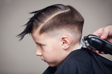Hairdresser making a haircut to a boy with clipper. - 209583476