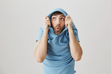 Positive funny european male pulling shirt on head and staring through collar up as if seeing some...