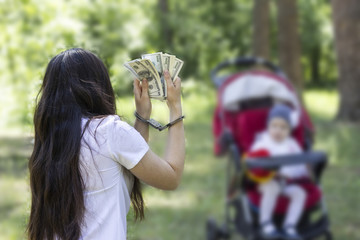A girl is holding money dollars in handcuffs against the backdrop of a baby in a carriage, arrest, detention for sale by children, trafficking in children