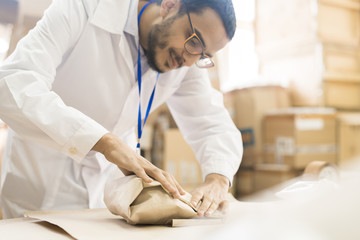 Young Arabian worker wearing lab coat and eyeglasses wrapped up in work at packaging department of...