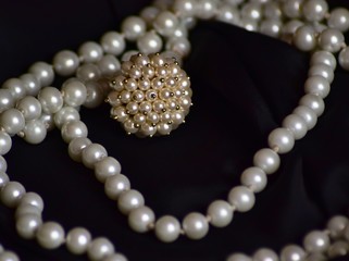 Ring and necklace of white pearls lie on black fabric.