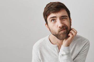 Obraz premium Man do not know how to solve problem. Indoor shot of clueless troubled european guy looking up and squinting, scratching beard while making calculations in mind, standing over gray background