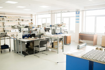 Spacious production department of measuring device factory: male workers sitting at desks and assembling pressure transducers, panoramic windows, spare parts lying everywhere