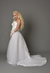 full length portrait of blonde  girl wearing white fantasy gown. standing pose in side profile, grey studio background.